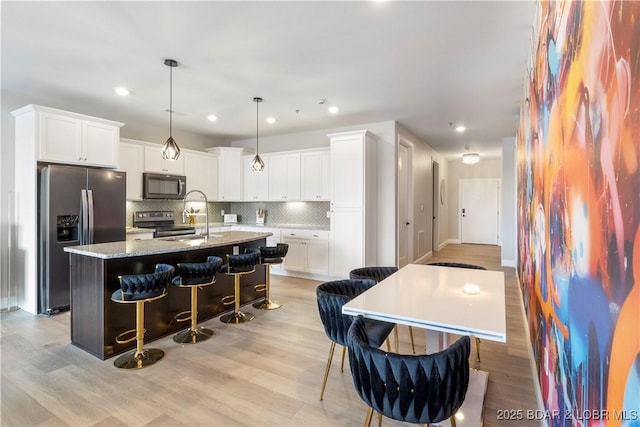 kitchen with tasteful backsplash, appliances with stainless steel finishes, a kitchen breakfast bar, a kitchen island with sink, and a sink