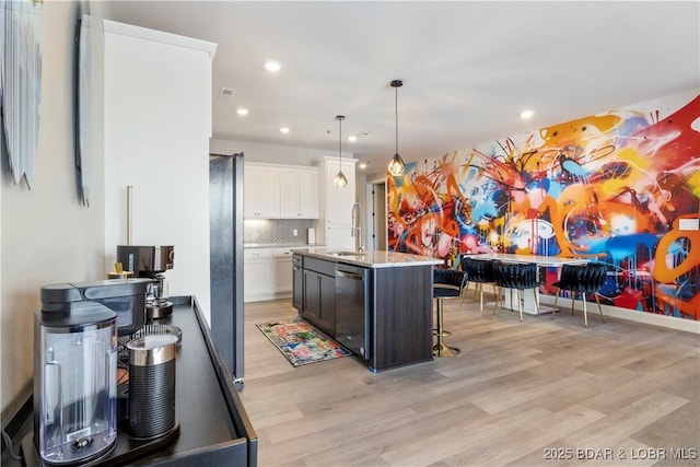 kitchen featuring light stone counters, stainless steel appliances, a sink, light wood-style floors, and tasteful backsplash