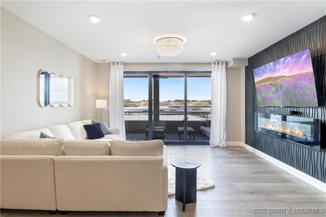 living area featuring a glass covered fireplace, recessed lighting, wood finished floors, and baseboards