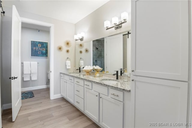 full bathroom featuring double vanity, baseboards, tiled shower, wood finished floors, and a sink