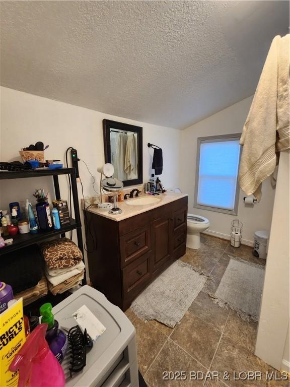 bathroom featuring vanity, toilet, vaulted ceiling, and a textured ceiling