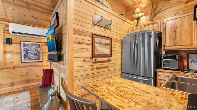 kitchen featuring butcher block countertops, stainless steel refrigerator, wood walls, an AC wall unit, and light brown cabinets