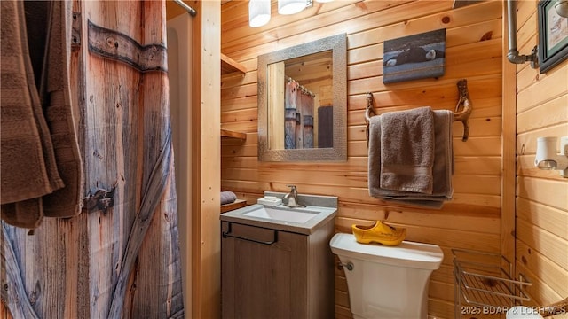 bathroom with vanity, toilet, and wood walls