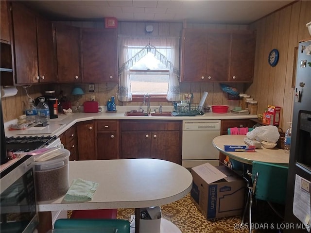 kitchen featuring appliances with stainless steel finishes, wooden walls, tasteful backsplash, sink, and dark brown cabinetry