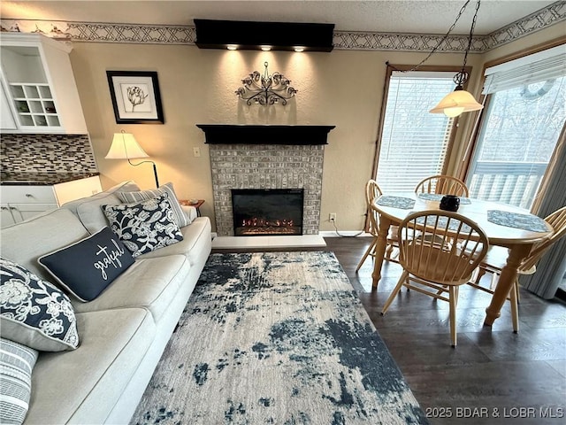 living area featuring dark wood-style floors, a brick fireplace, a textured ceiling, and baseboards