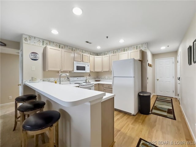 kitchen featuring light wood-type flooring, kitchen peninsula, a breakfast bar, sink, and white appliances