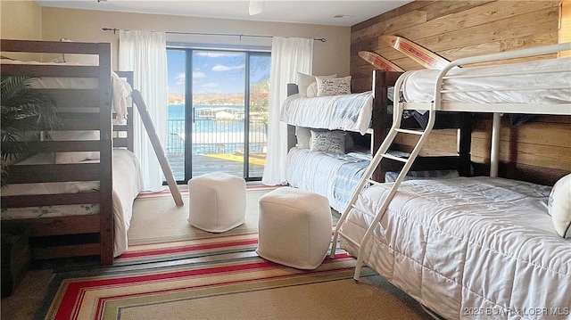 bedroom with a water view, access to outside, and wood walls