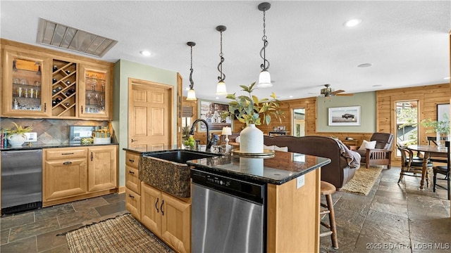 kitchen with a kitchen island with sink, hanging light fixtures, a breakfast bar, dishwasher, and wooden walls