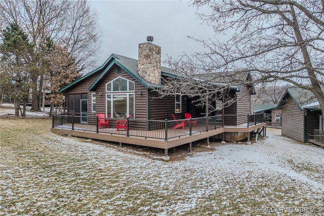 snow covered house featuring faux log siding, a chimney, and a deck