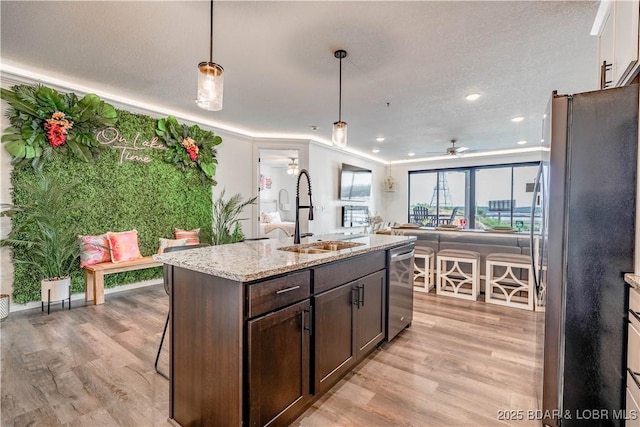 kitchen with light stone counters, hanging light fixtures, stainless steel appliances, dark brown cabinets, and a sink