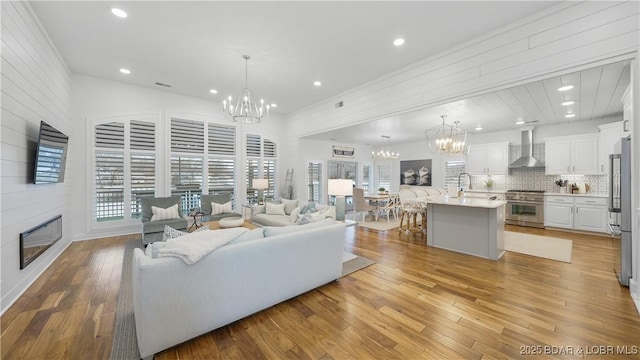 living area featuring light wood-type flooring, a large fireplace, recessed lighting, and an inviting chandelier