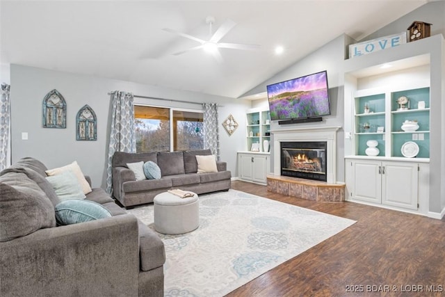 living area with lofted ceiling, a glass covered fireplace, wood finished floors, and built in shelves