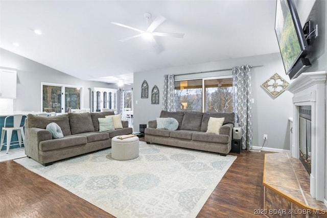 living room with wood finished floors, a ceiling fan, baseboards, vaulted ceiling, and a glass covered fireplace