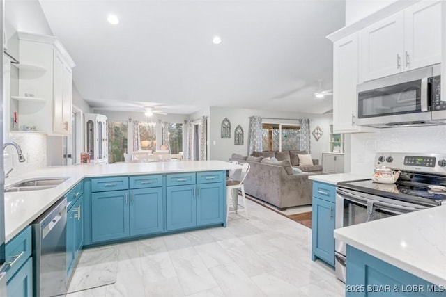 kitchen featuring stainless steel appliances, a sink, a ceiling fan, open floor plan, and blue cabinetry