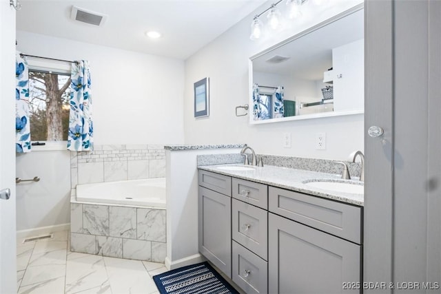 full bathroom with double vanity, a garden tub, visible vents, and a sink