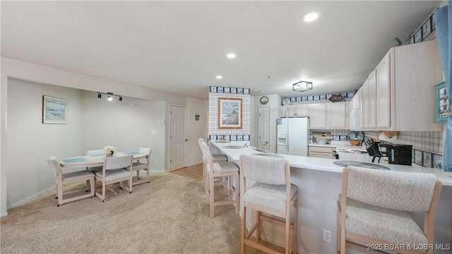 kitchen with white cabinets, light countertops, white fridge with ice dispenser, tasteful backsplash, and a kitchen bar