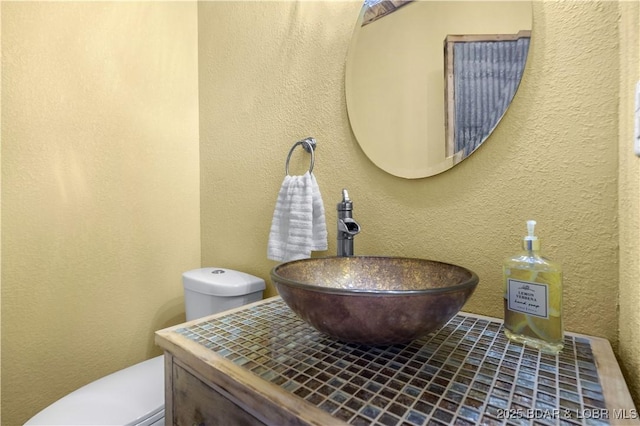 half bathroom with a textured wall, vanity, and toilet