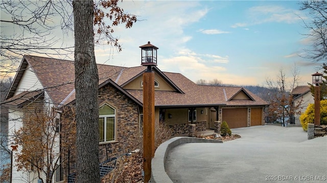 view of front of home featuring an attached garage, stone siding, a shingled roof, and concrete driveway