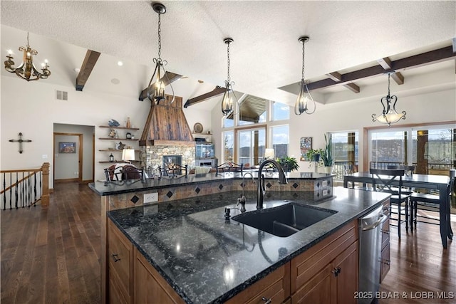 kitchen with a center island with sink, dark stone counters, a sink, and decorative light fixtures