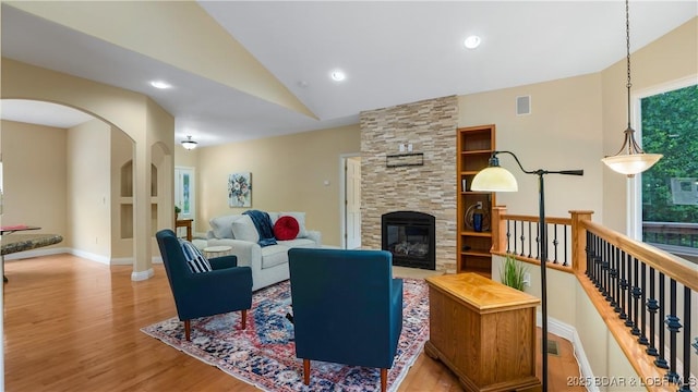 living area with arched walkways, a stone fireplace, visible vents, light wood-style floors, and vaulted ceiling