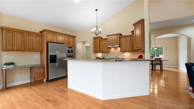 kitchen with arched walkways, stainless steel appliances, stone countertops, and brown cabinets