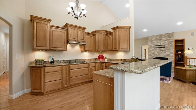 kitchen with arched walkways, black electric stovetop, under cabinet range hood, a peninsula, and pendant lighting