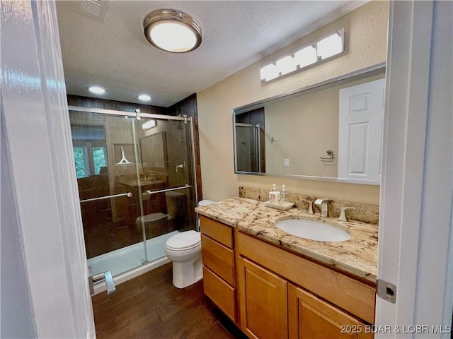 bathroom with a textured ceiling, toilet, wood finished floors, vanity, and a shower stall