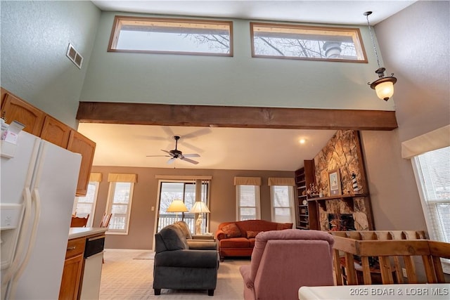 living room featuring a wealth of natural light, visible vents, beamed ceiling, and a stone fireplace