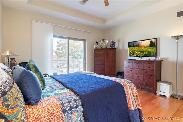 bedroom with light wood-style floors, a raised ceiling, a ceiling fan, and access to exterior