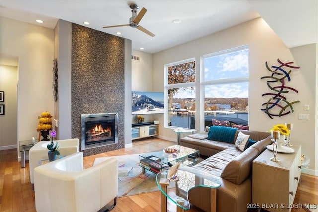 living area with a fireplace, light wood finished floors, visible vents, ceiling fan, and baseboards