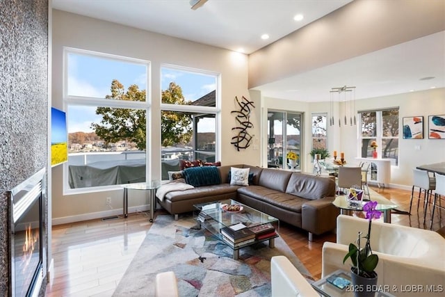 living room featuring a glass covered fireplace, baseboards, recessed lighting, and wood finished floors