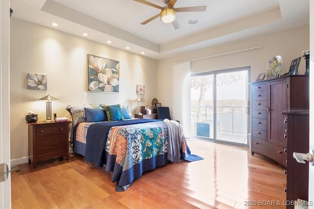 bedroom with access to outside, a raised ceiling, and light wood-style floors