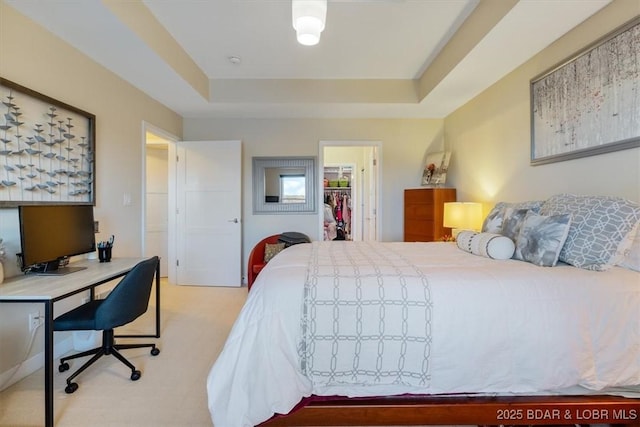 bedroom featuring a tray ceiling, a walk in closet, and light colored carpet