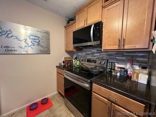 kitchen with a textured ceiling, baseboards, appliances with stainless steel finishes, decorative backsplash, and dark stone countertops