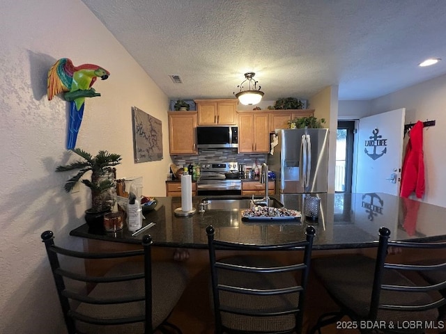 kitchen with dark countertops, appliances with stainless steel finishes, a peninsula, a sink, and backsplash