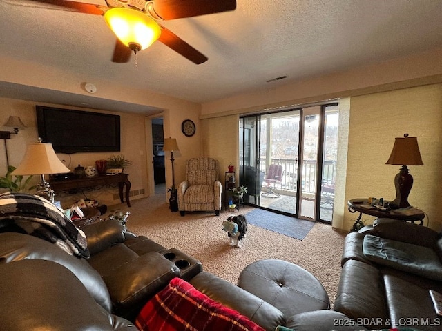 carpeted living room with a textured ceiling, visible vents, and a ceiling fan