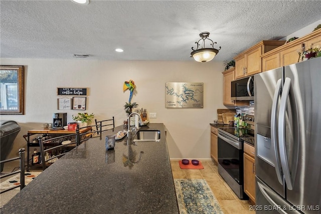 kitchen featuring dark stone counters, stainless steel appliances, a textured ceiling, pendant lighting, and a sink