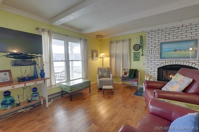 living area featuring a fireplace, beamed ceiling, a textured ceiling, and wood finished floors