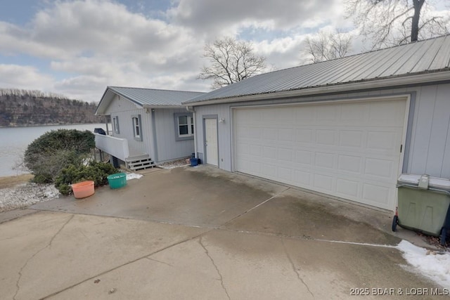 view of front of home with a water view, a garage, metal roof, and concrete driveway