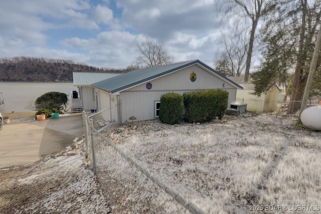 view of side of property with metal roof, a water view, and fence