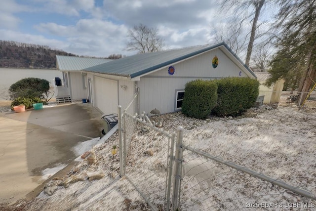 view of side of home featuring metal roof, a garage, a water view, fence, and driveway