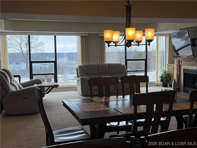 carpeted dining area with a tile fireplace, plenty of natural light, and an inviting chandelier