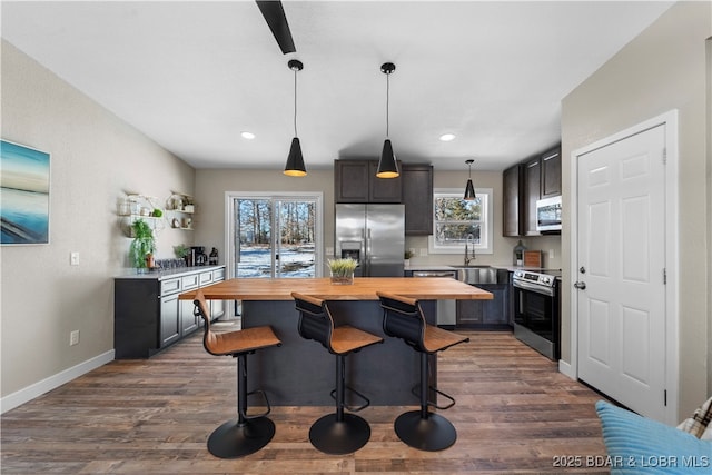 kitchen featuring butcher block countertops, dark wood-type flooring, a center island, stainless steel appliances, and pendant lighting