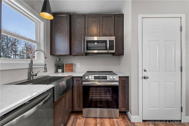 kitchen featuring light countertops, appliances with stainless steel finishes, dark brown cabinetry, a sink, and wood finished floors