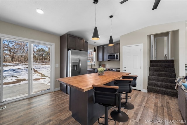 kitchen with pendant lighting, appliances with stainless steel finishes, dark brown cabinets, butcher block countertops, and a kitchen bar