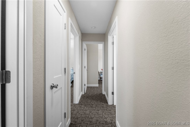 hall with dark colored carpet, a textured wall, and baseboards