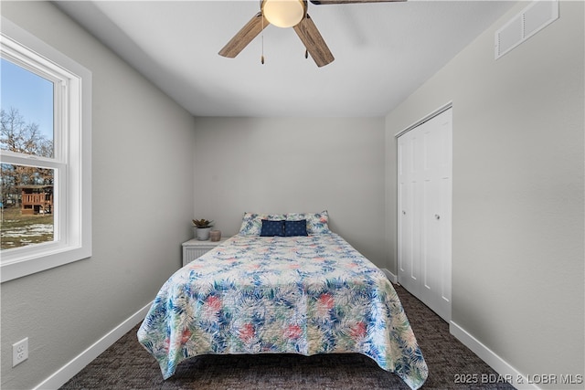 bedroom with baseboards, visible vents, ceiling fan, dark carpet, and a closet