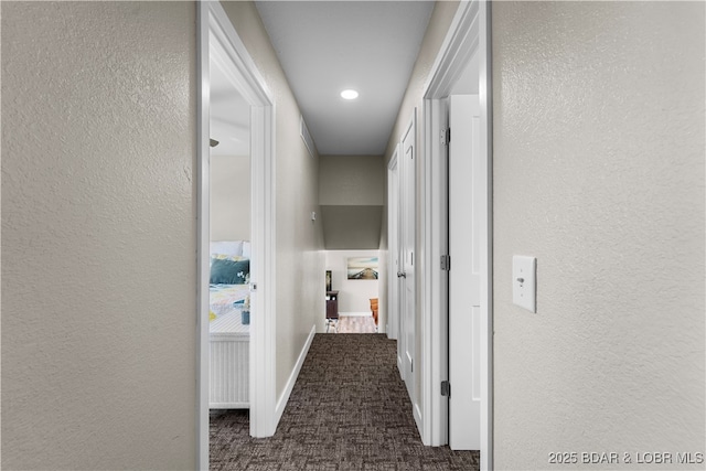 hallway with a textured wall, dark carpet, and baseboards