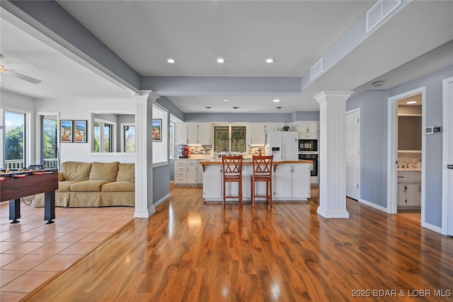 kitchen featuring open floor plan, white refrigerator with ice dispenser, decorative columns, and white cabinets