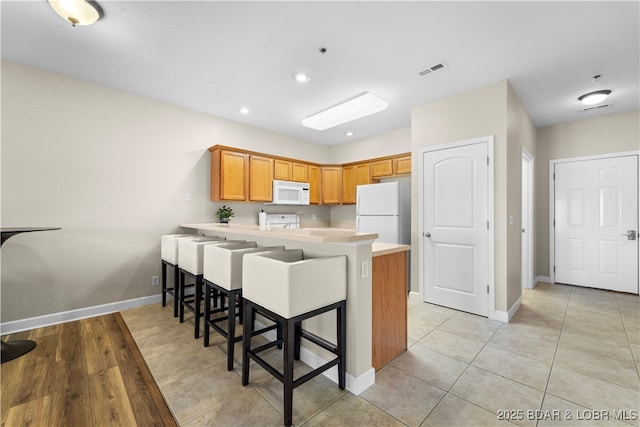 kitchen with a breakfast bar area, visible vents, light countertops, white appliances, and a peninsula